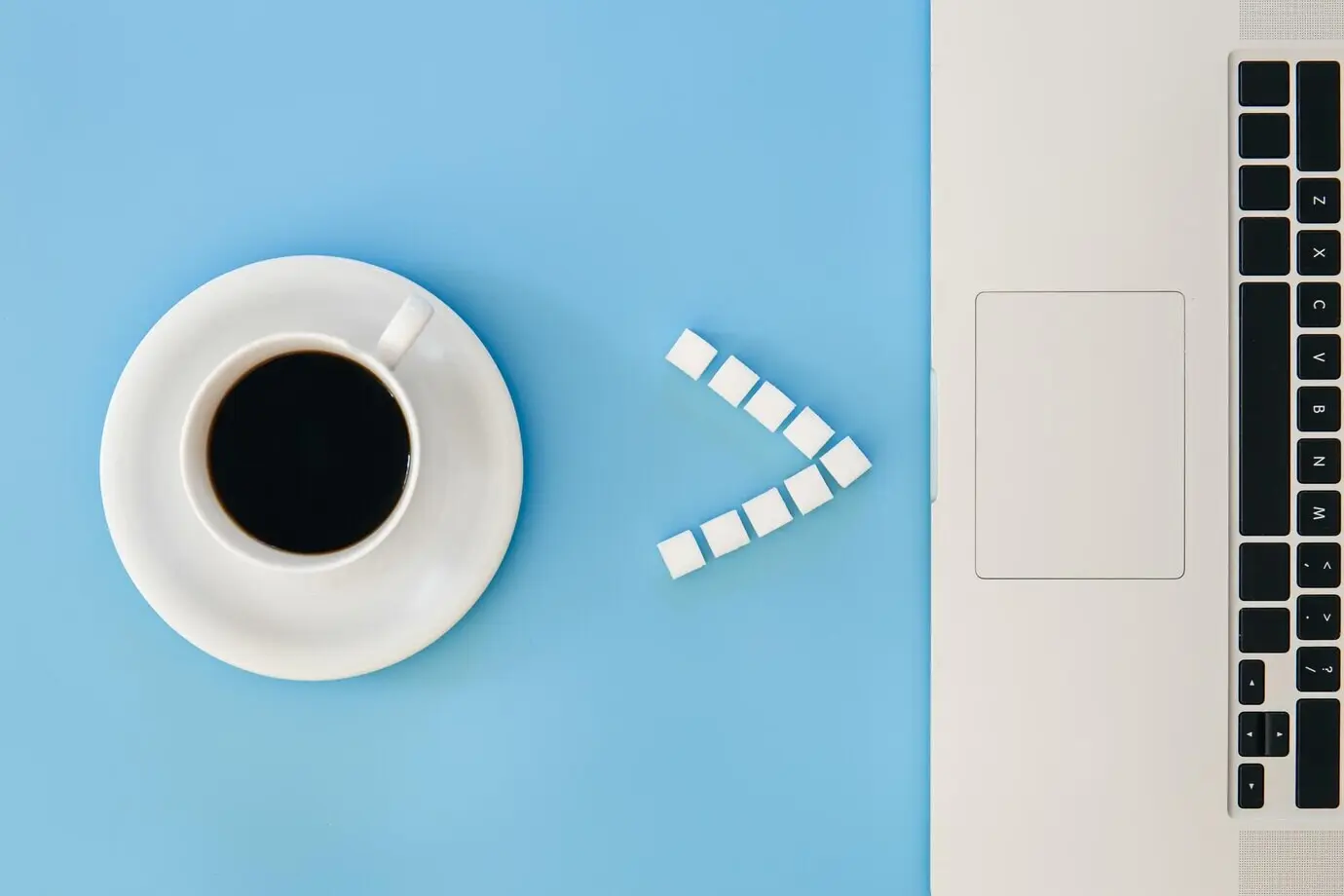 Flat lay of a coffee cup and a laptop on a blue background