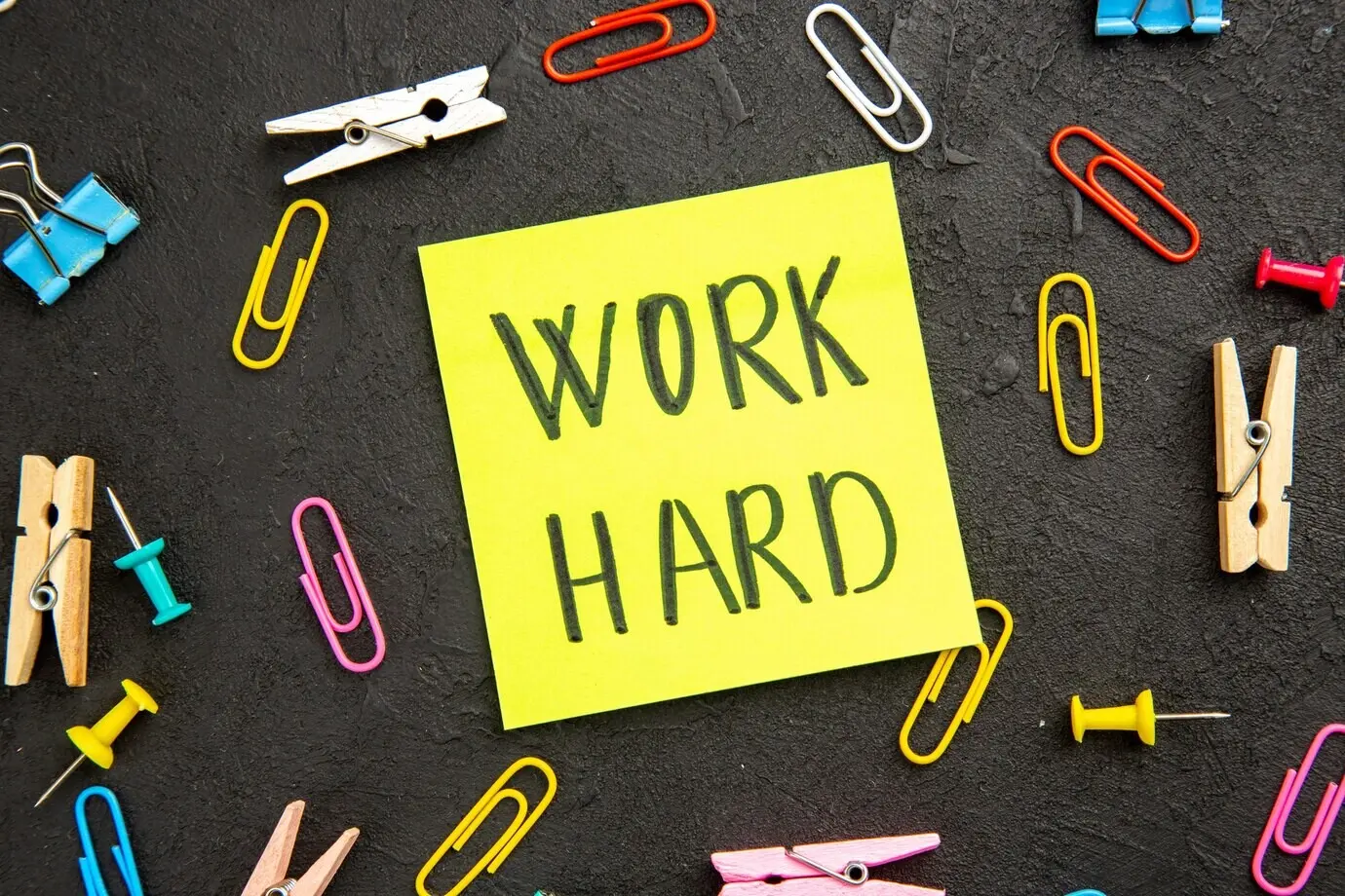 Overhead view of a motivational note with clothespins and staples on the dark surface