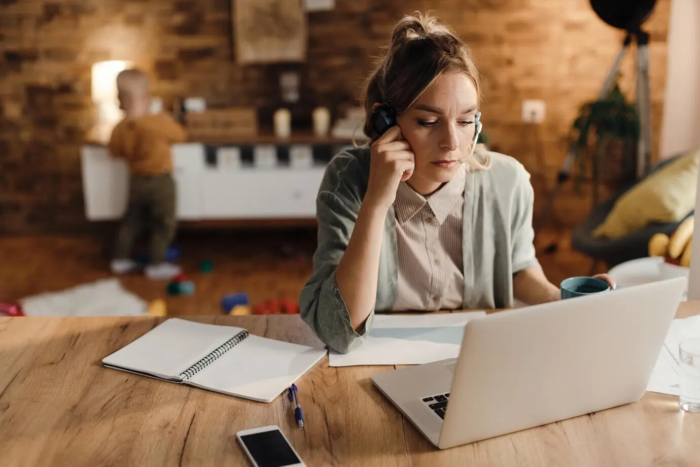 A stay-at-home mother works on a computer while her son plays in the background.