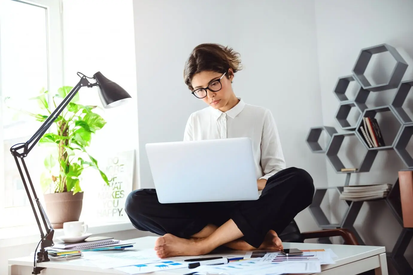 At a workplace, a young, beautiful businesswoman sits on a table with a laptop.