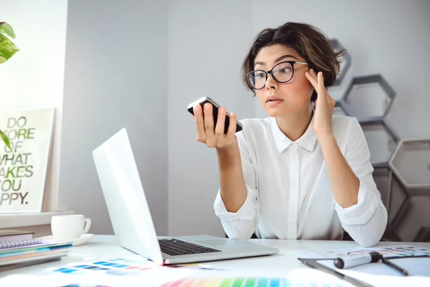 A young, beautiful businesswoman looking at a phone at an office workplace.